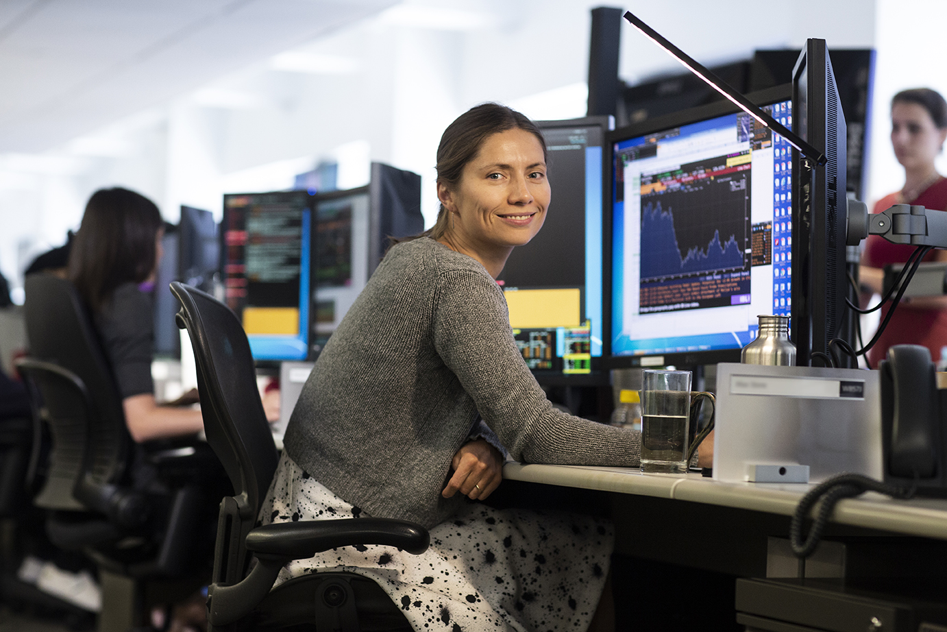 Woman sitting at her workstation smiling at the camera on the trading floor.
